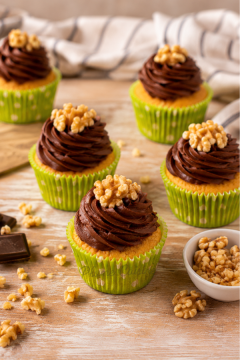 Cupcakes vanille et glaçage chocolat sur une table en bois dans une ambiance lumineuse et gourmande.