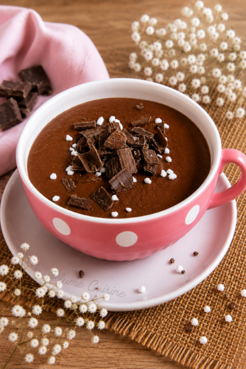 Crème au chocolat maison servie dans une tasse rose à pois blancs, garnie de copeaux de chocolat.