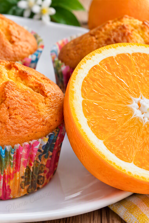 Gros plan sur une tranche d'orange fraîche et juteuse posée à côté de muffins artisanaux à l'orange.
