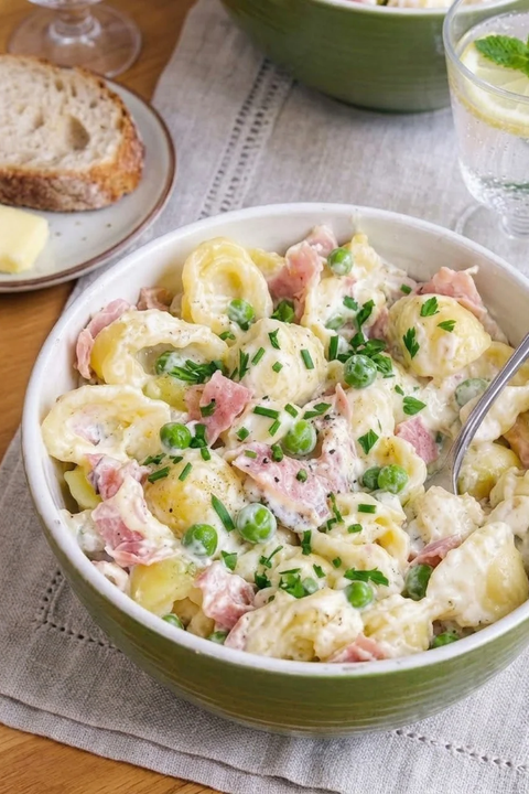 Photo en gros plan d'un bol de pâtes conchiglie crémeuses au jambon, petits pois et ciboulette fraîche.