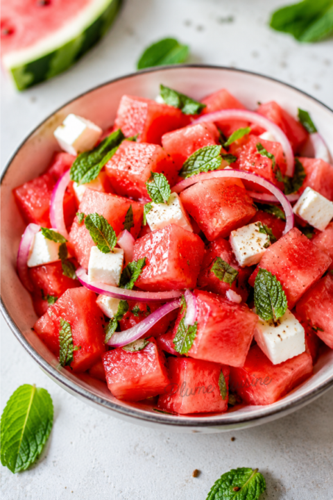Salade de pastèque, feta et menthe fraîche servie dans un bol, avec de fines lamelles d’oignon rouge et une vinaigrette légère, 