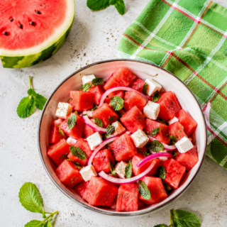 Vue d’ensemble d’une salade fraîche de pastèque, feta, menthe et oignon rouge, présentée dans une ambiance estivale lumineuse