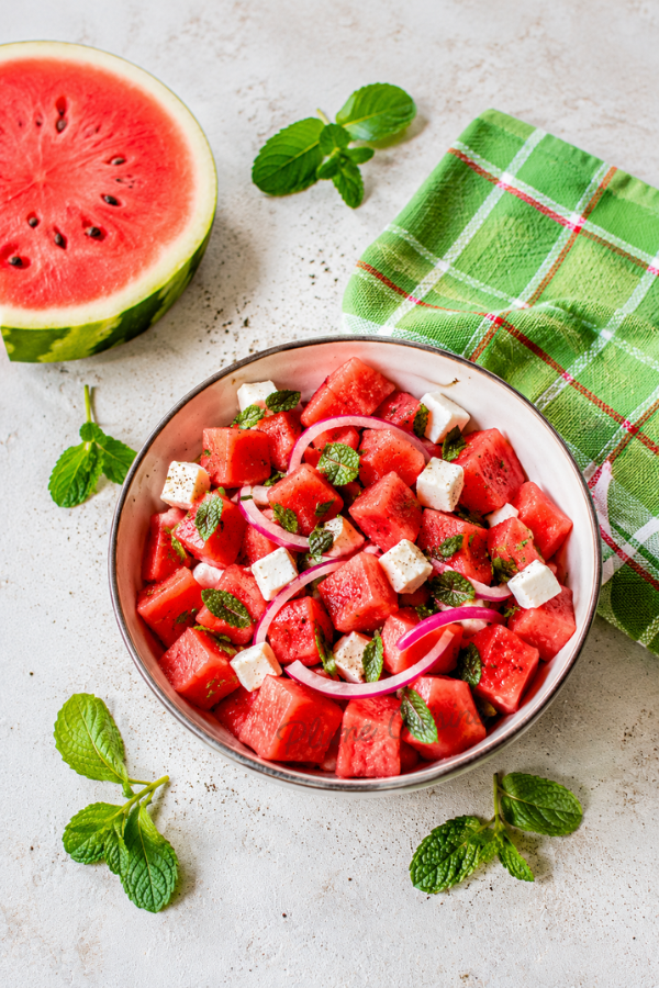 Vue d’ensemble d’une salade fraîche de pastèque, feta, menthe et oignon rouge, présentée dans une ambiance estivale lumineuse