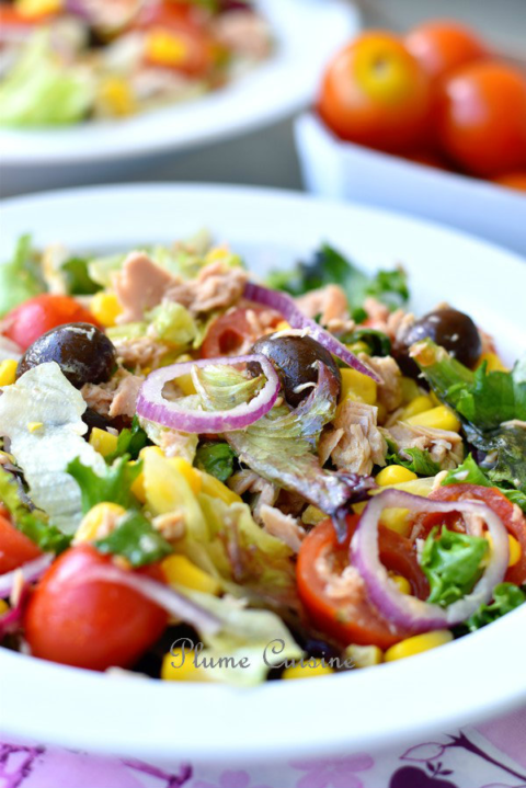 Salade de thon rapide servie dans des assiettes blanches avec tomates, maïs, olives noires, laitue et oignon rouge.