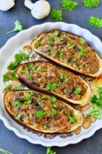 Plat à tarte blanc contenant trois moitiés d'aubergines farcies aux champignons.