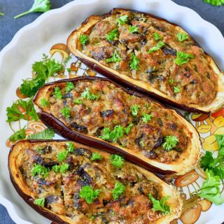 Plat à tarte blanc contenant trois moitiés d'aubergines farcies aux champignons.