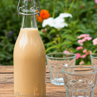 Bouteille de punch cacahuète antillais sur une table de jardin, avec trois verres et quelques cacahuètes avec leur coque en guise de décoration.