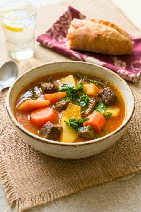 Bol de soupe de bœuf aux légumes, garni de persil frais, servi avec du pain croustillant.